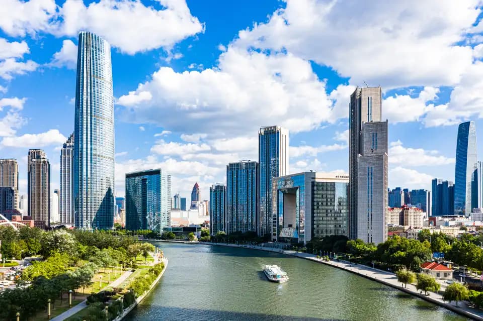 A sightseeing boat on the Haihe between green riverbanks and high-rise buildings in Tianjin by day.